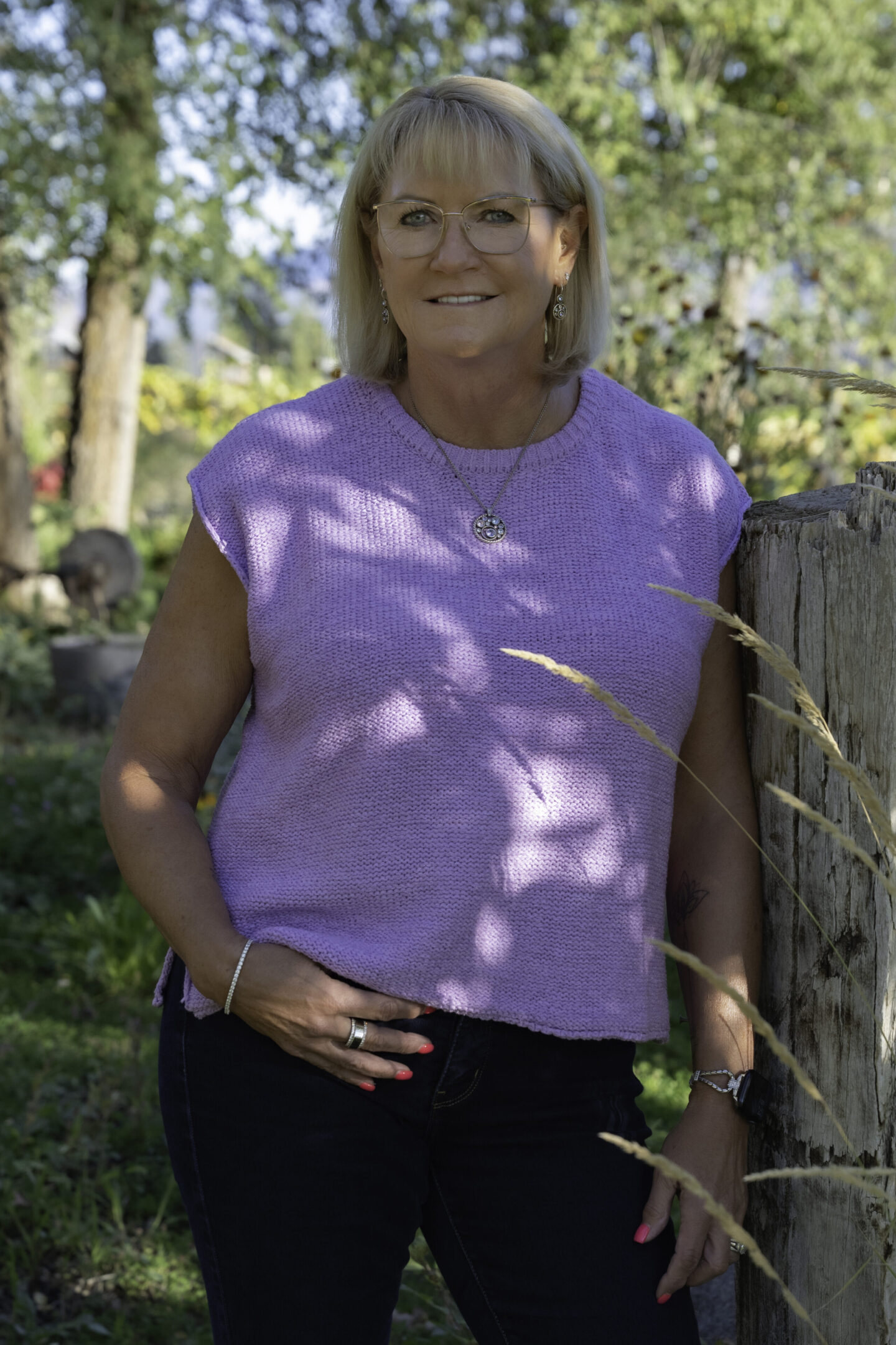 Woman wearing a purple sleeveless top, smiling outdoors.