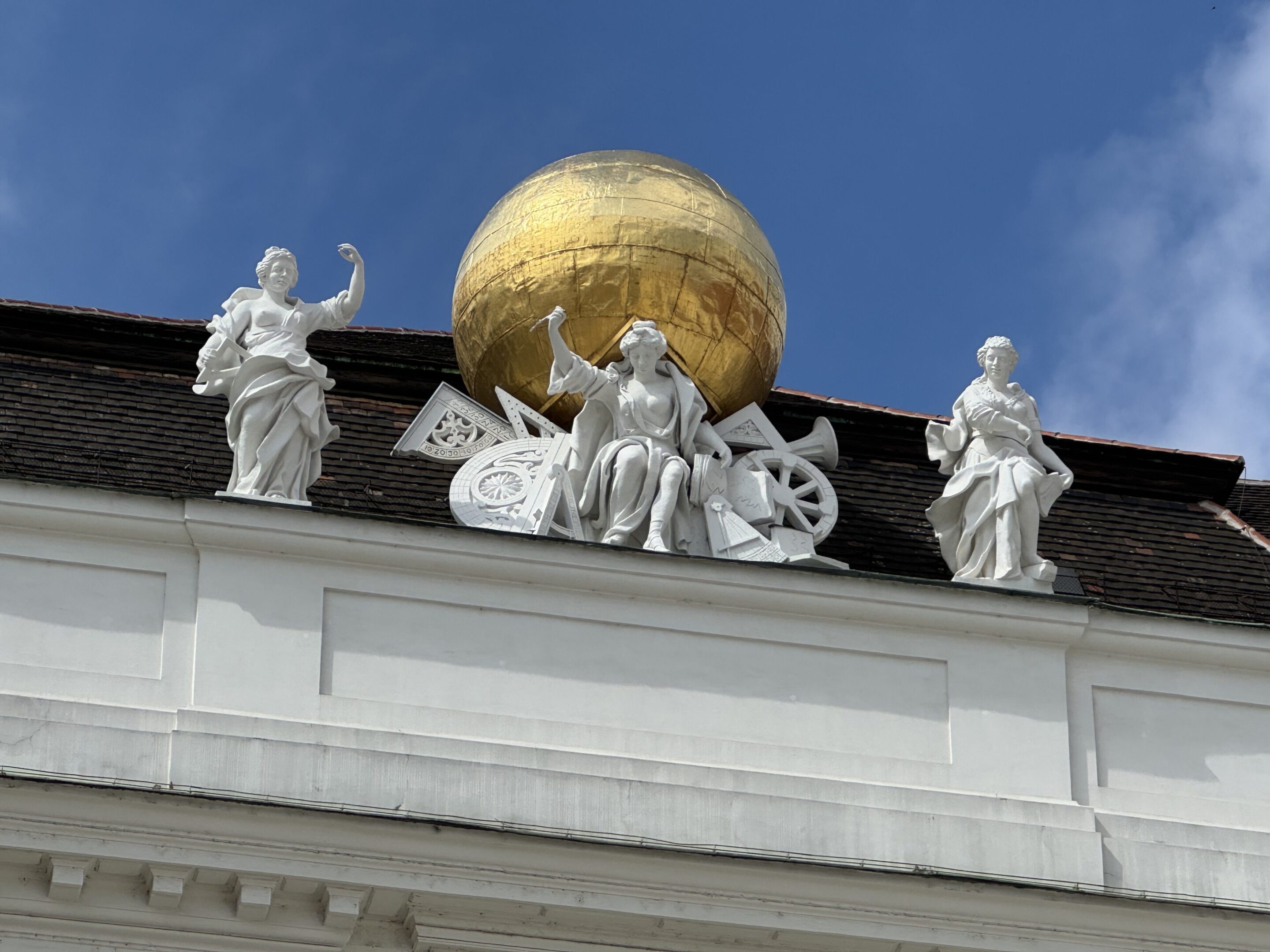 Sculptures of angels surrounding a golden globe atop a building under a clear blue sky.