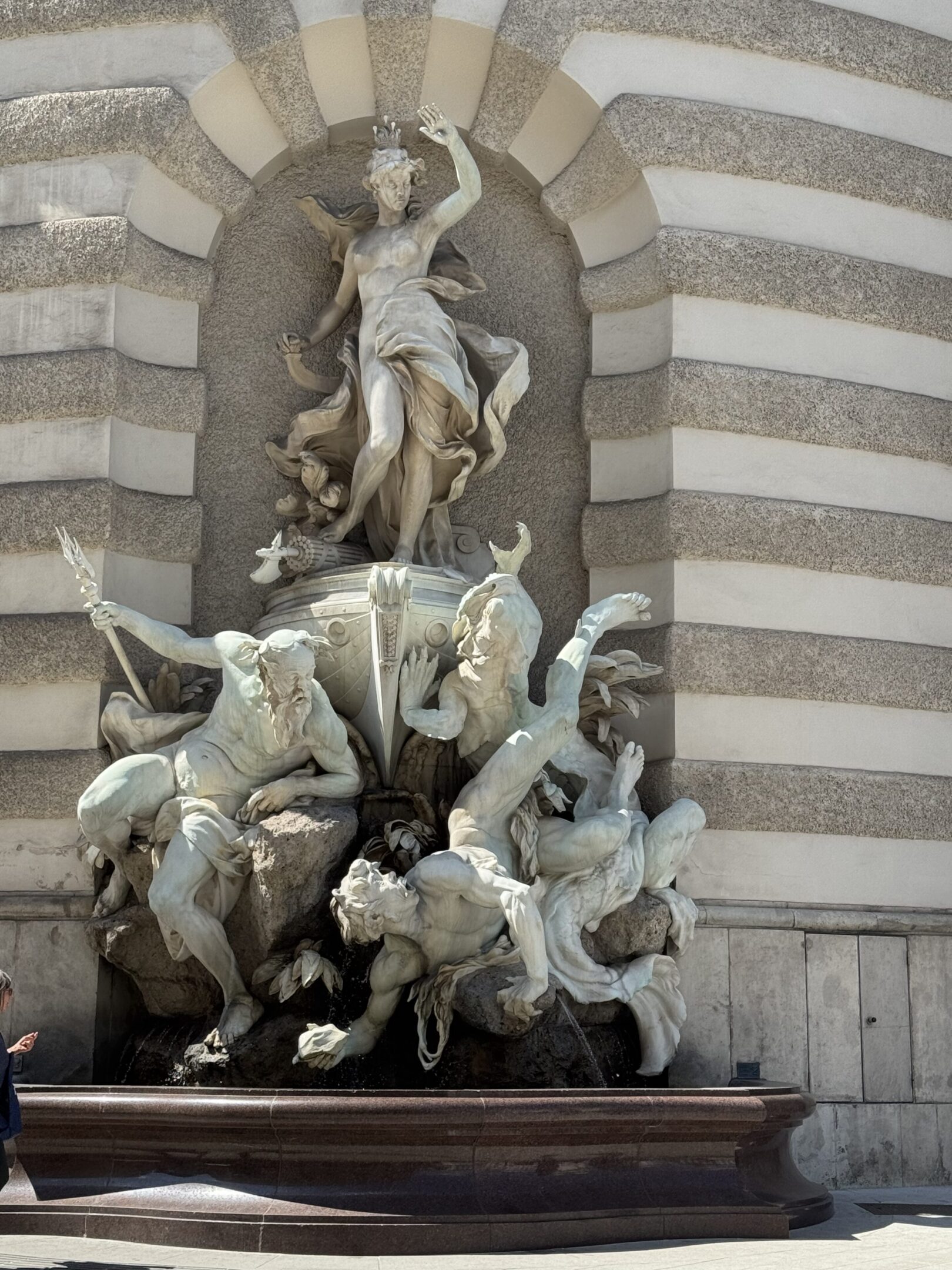 Intricate stone sculpture of mythical figures and horses on a striped building facade.