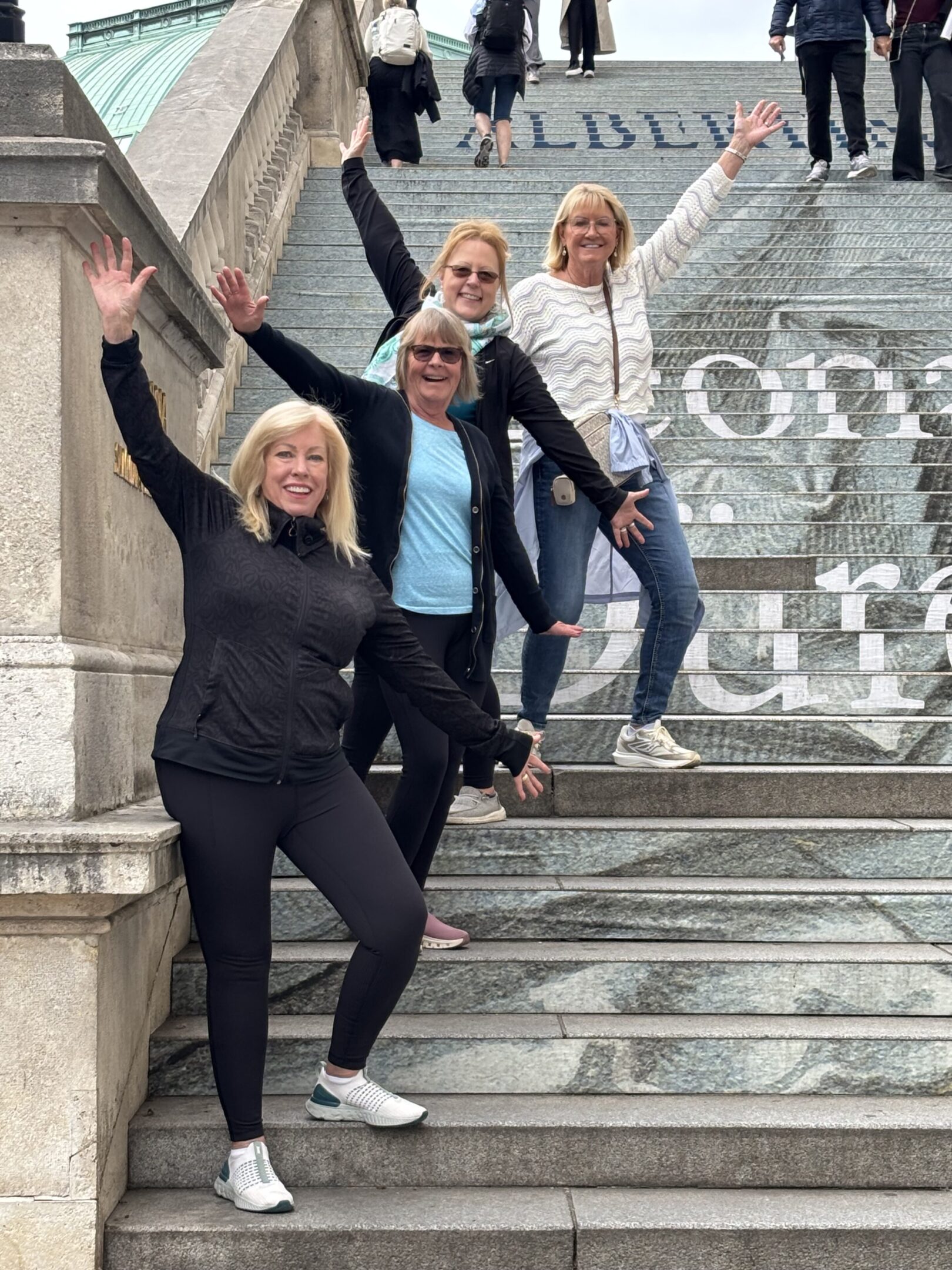 Four women posing joyfully on outdoor stairs with a large artistic backdrop.