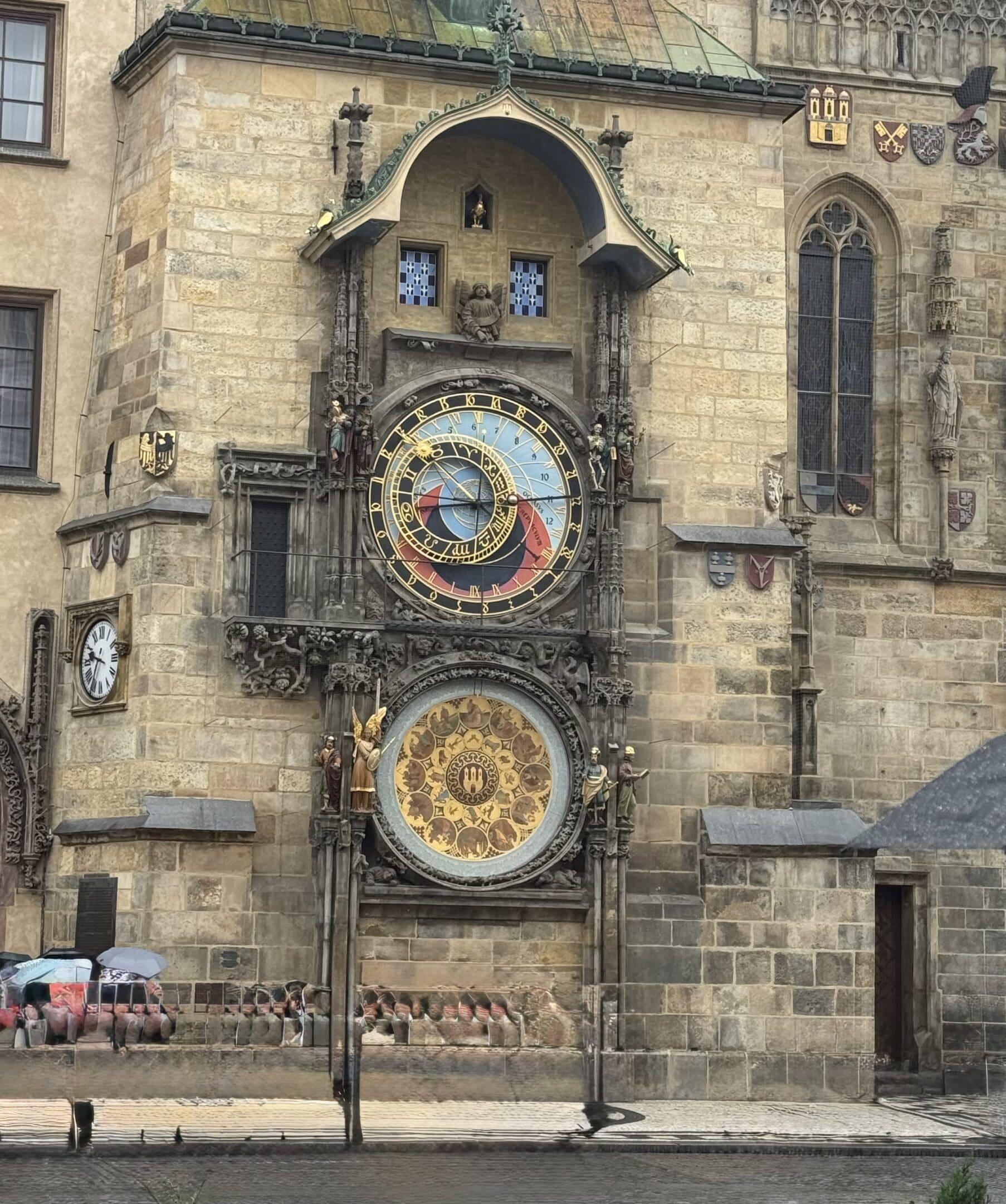 Historic astronomical clock on an old stone building in a city square.