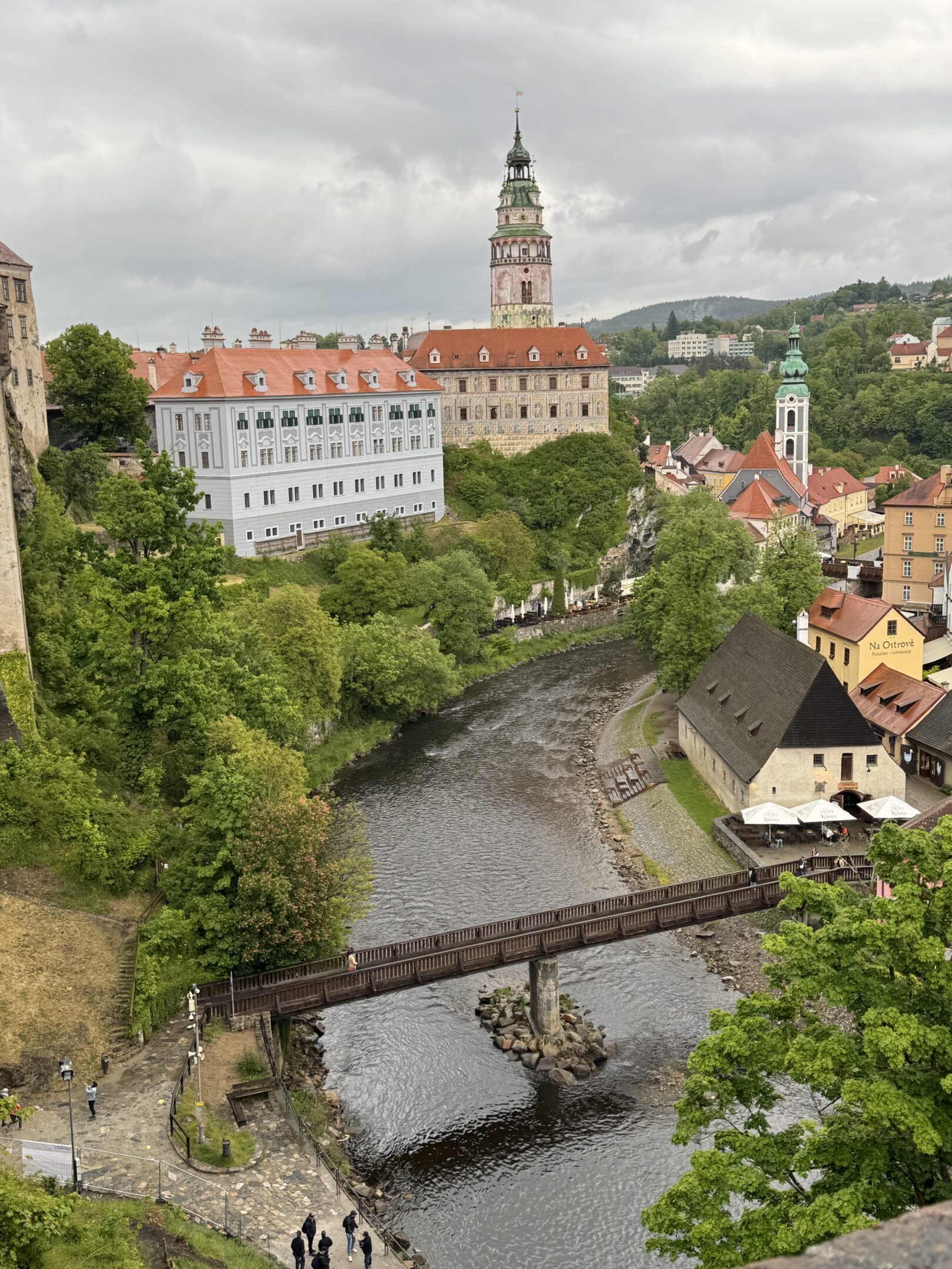 Scenic town with a river, bridge, and historic buildings under a cloudy sky.