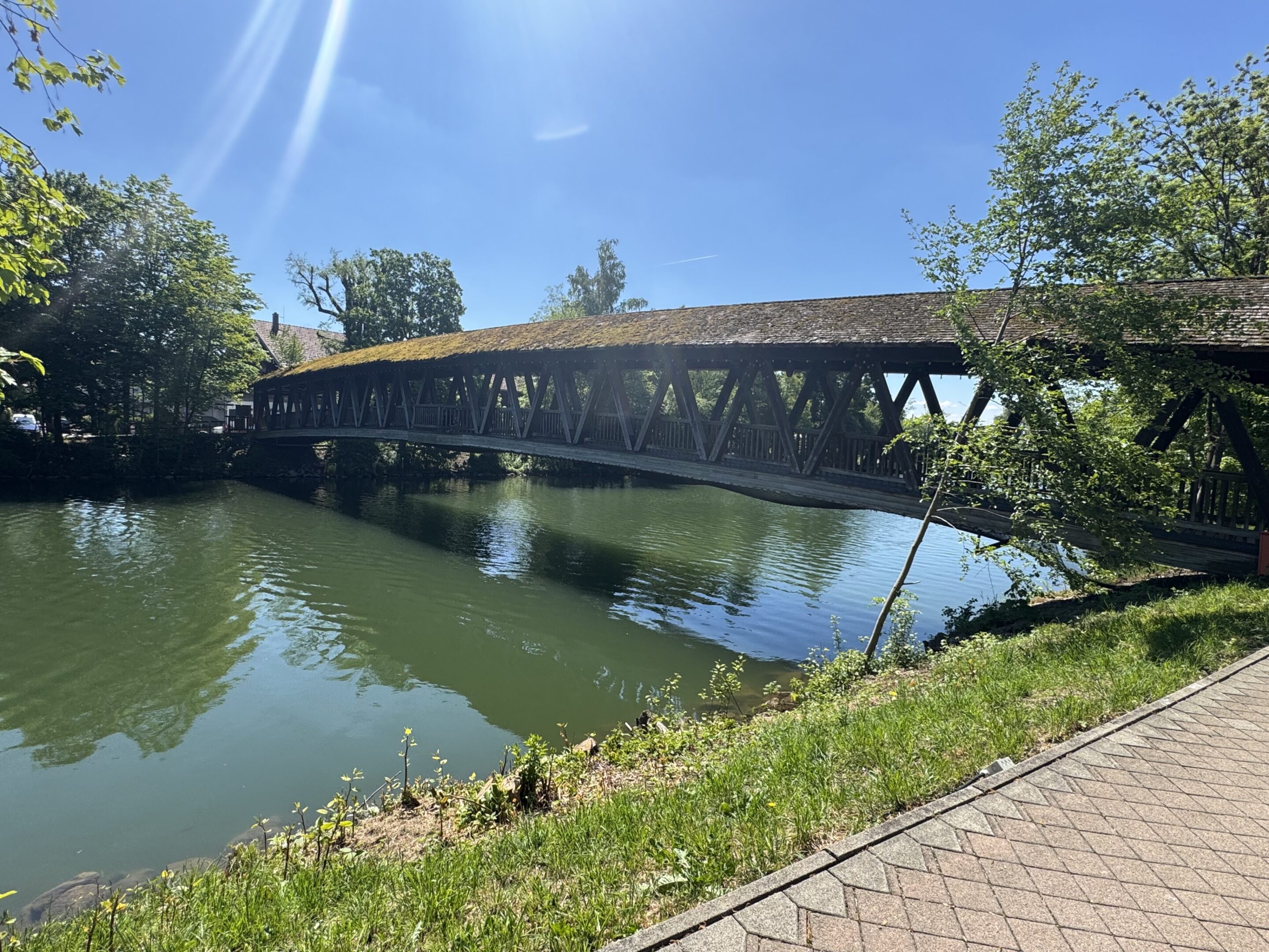 A wooden covered bridge over a calm river on a sunny day.