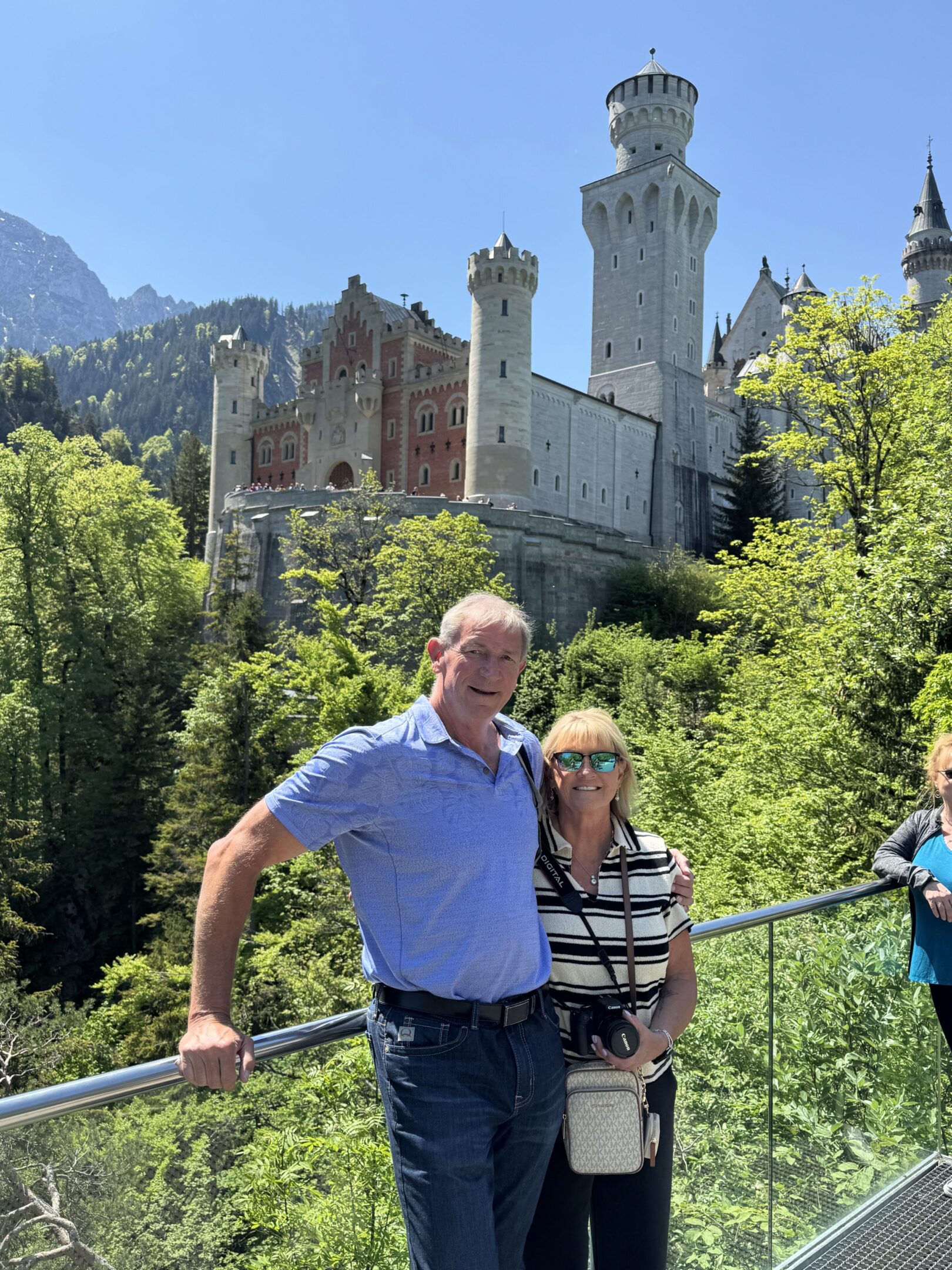 A couple posing in front of a majestic castle surrounded by greenery.