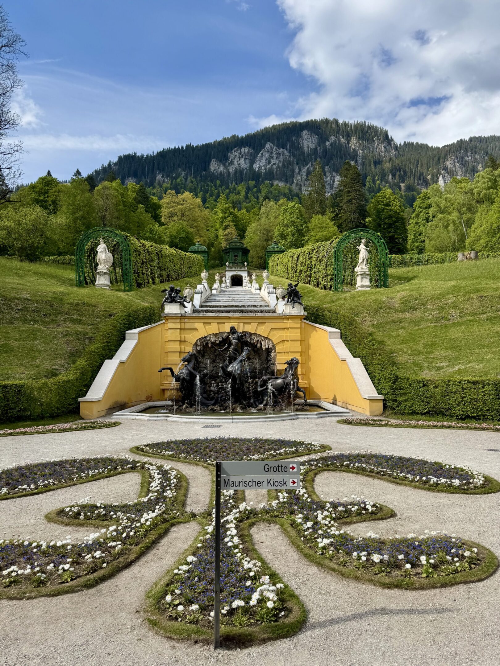 Elegant garden with ornate fountain and hillside backdrop.