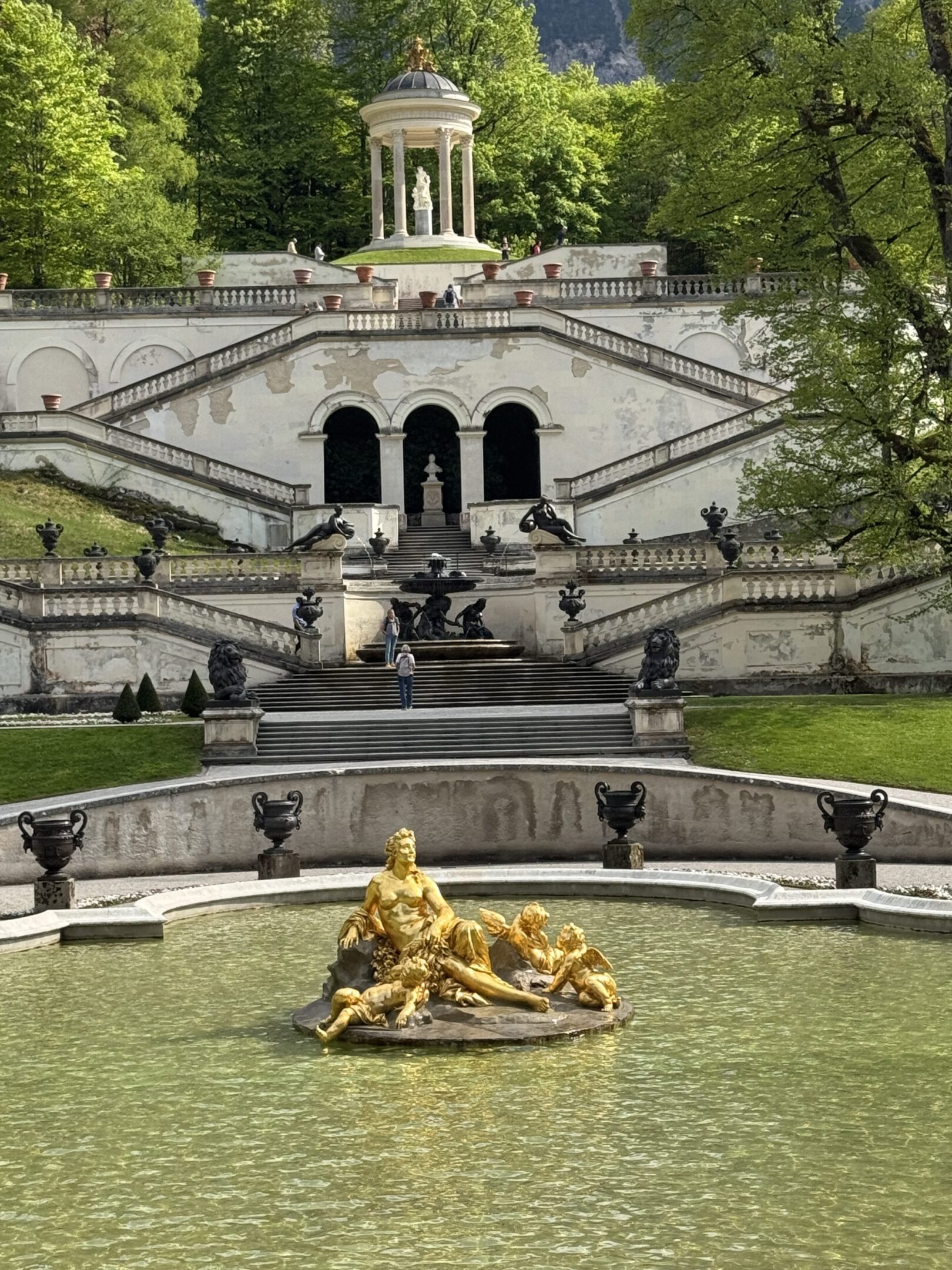 Ornate fountain and grand staircase in a lush garden.