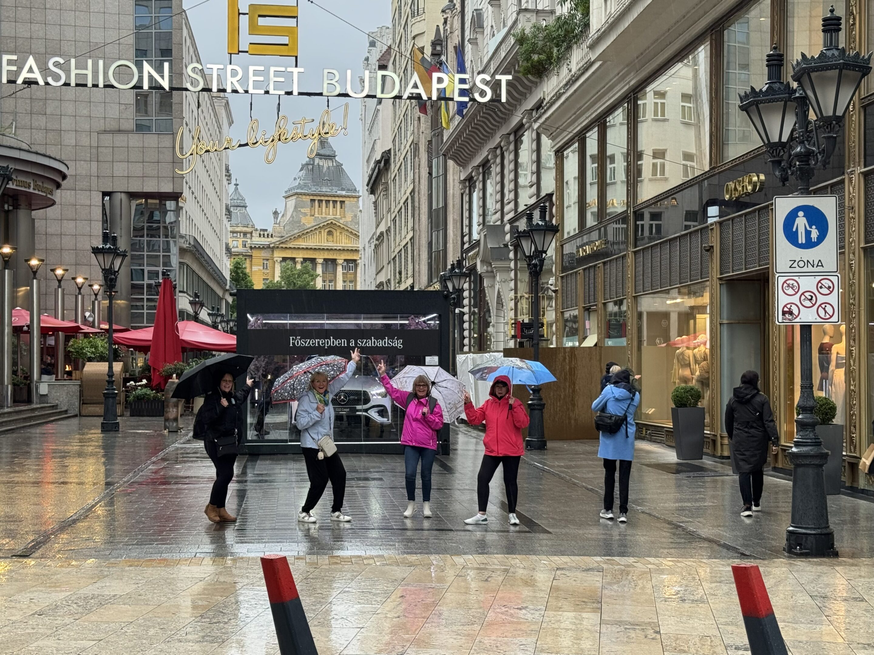 Children with colorful umbrellas walk on a rainy street in Budapest.