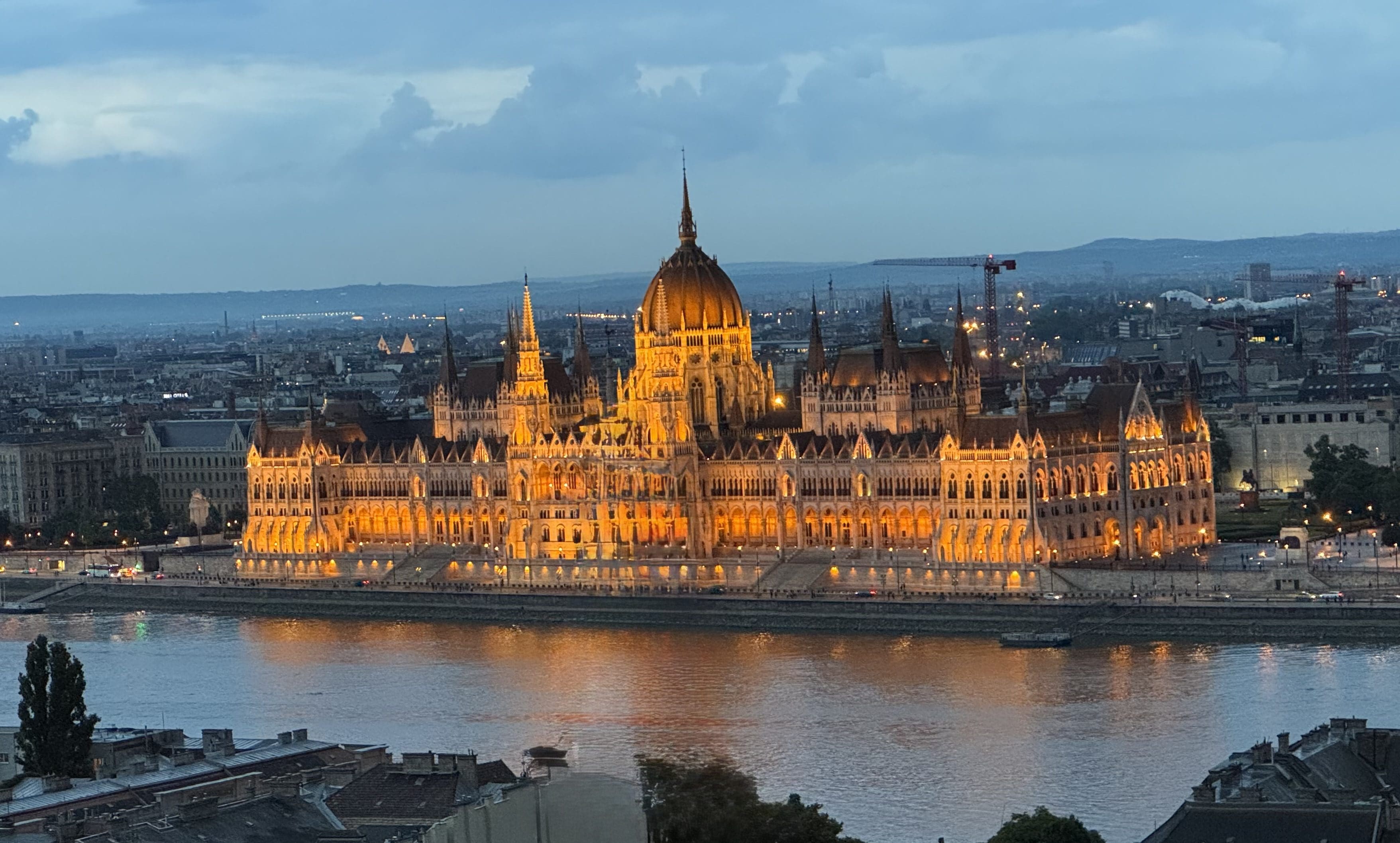 The illuminated Hungarian Parliament building at dusk along the Danube River.