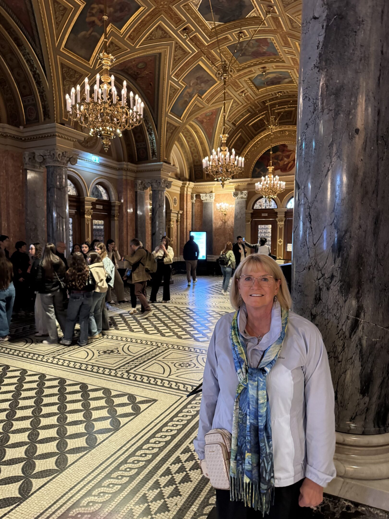 Woman posing inside an ornate historical building with a patterned floor and high vaulted ceilings.
