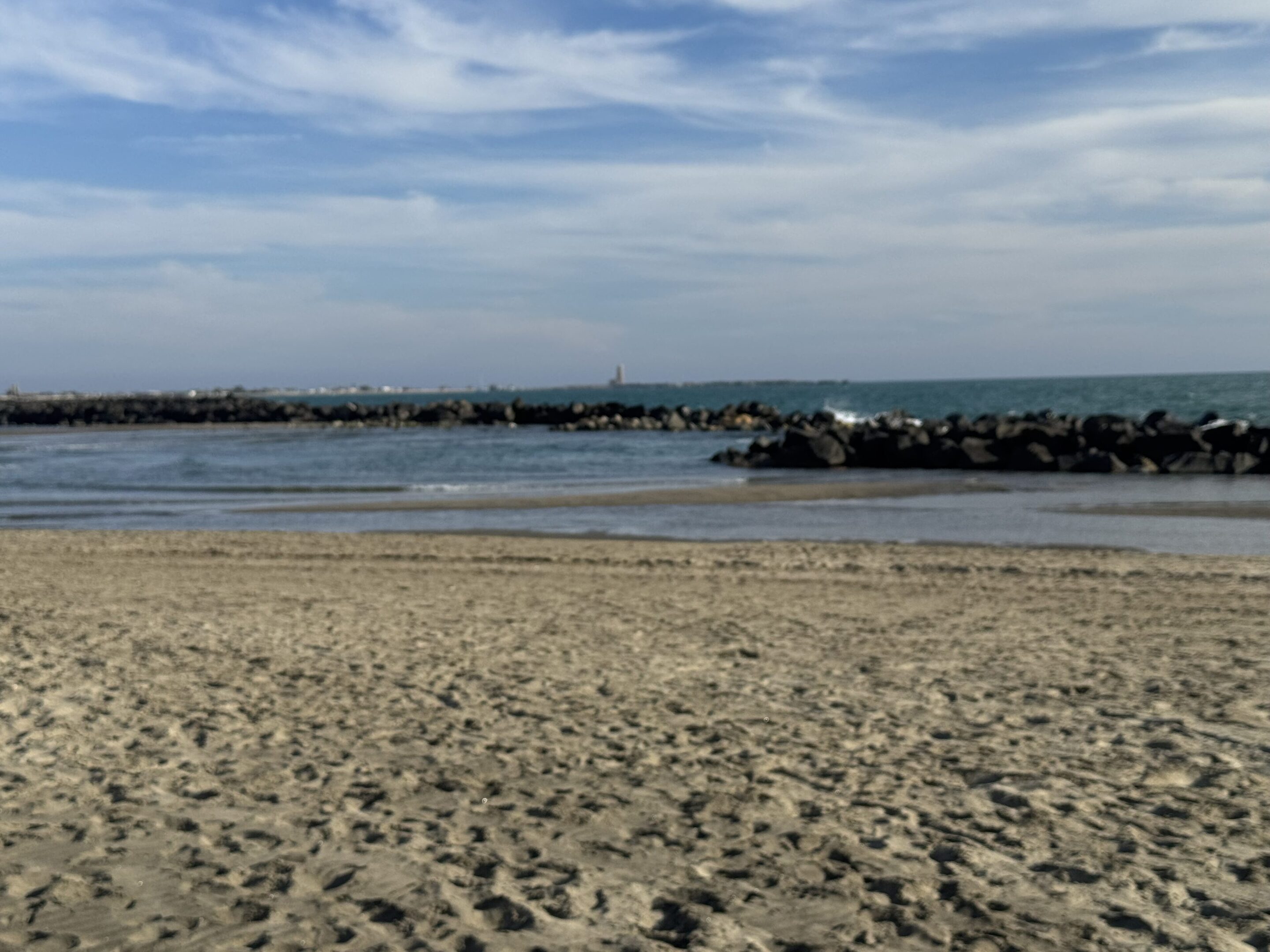Calm beach with sandy shore and gentle waves under a partly cloudy sky.