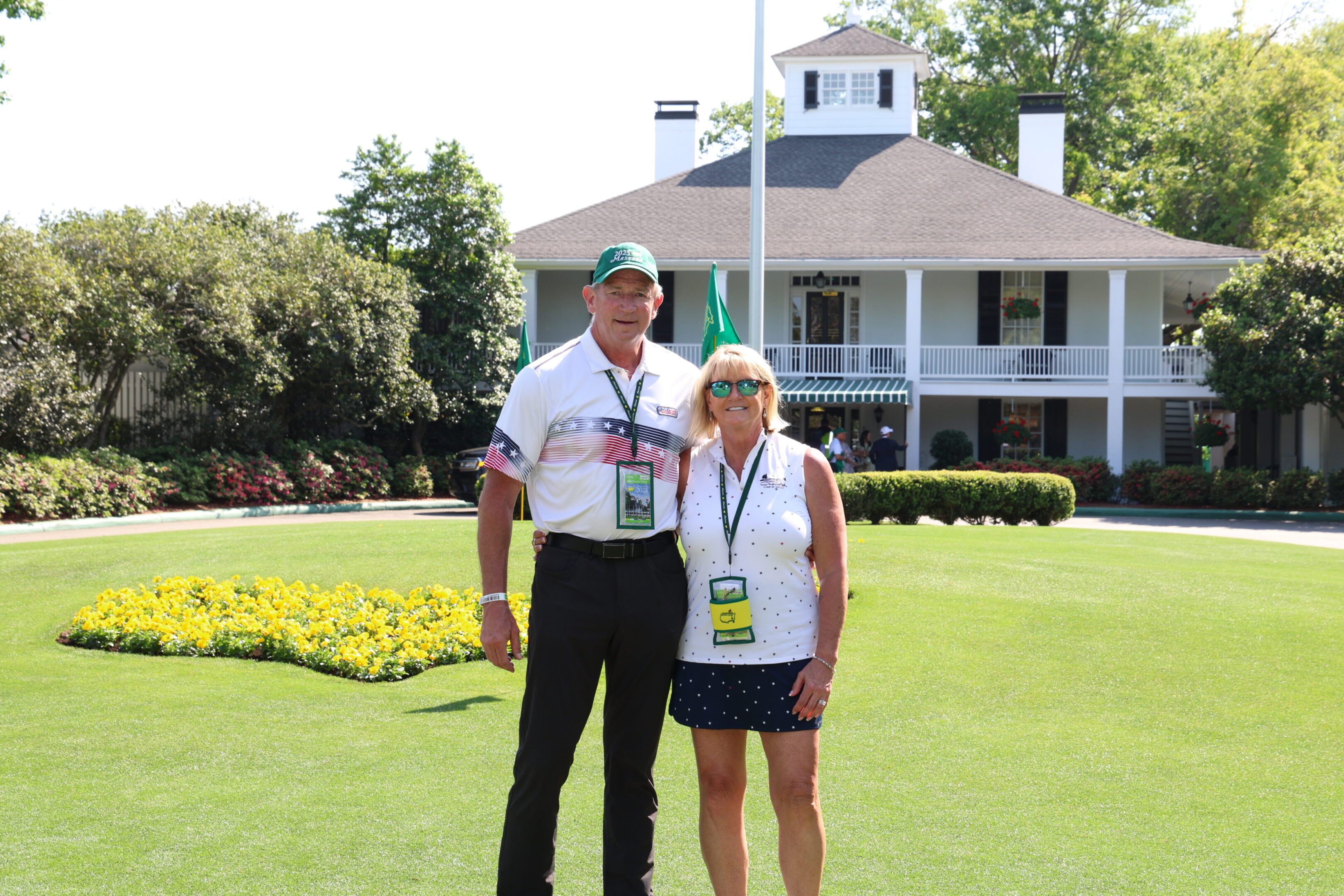 A smiling couple posing in front of a clubhouse on a sunny day.