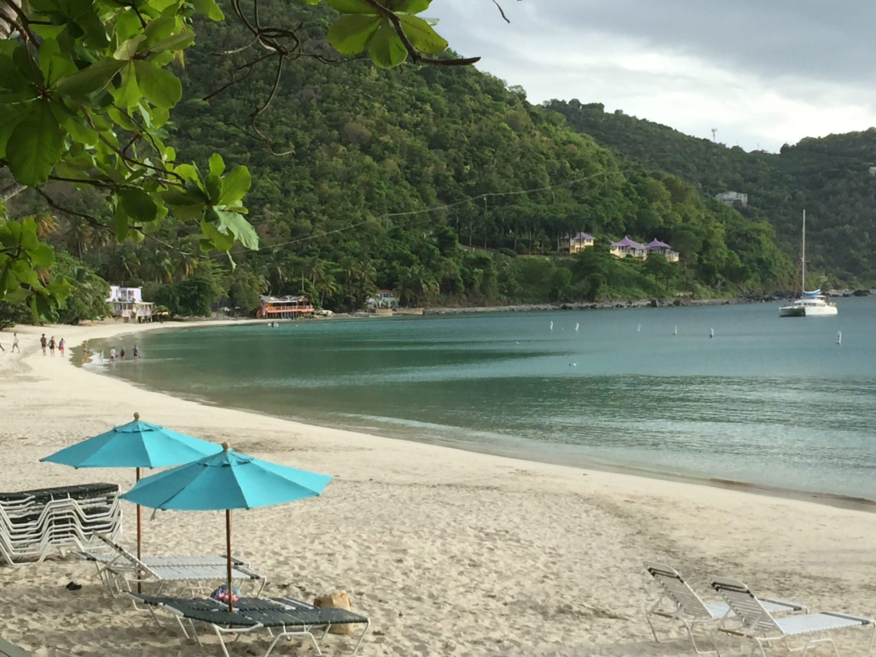 Serene beach with turquoise umbrellas and calm waters near green hills.