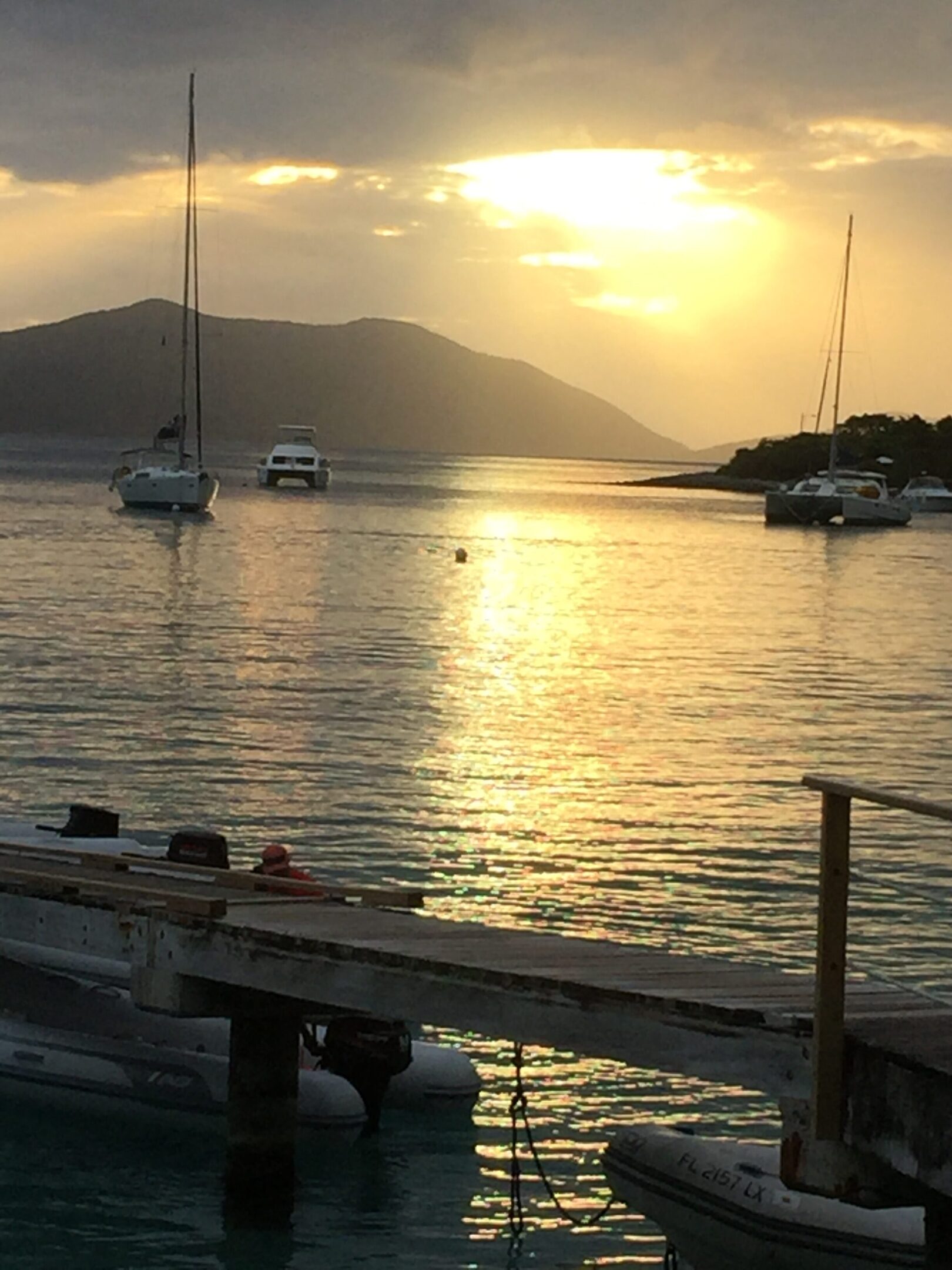 Sunset over calm waters with boats near a dock.