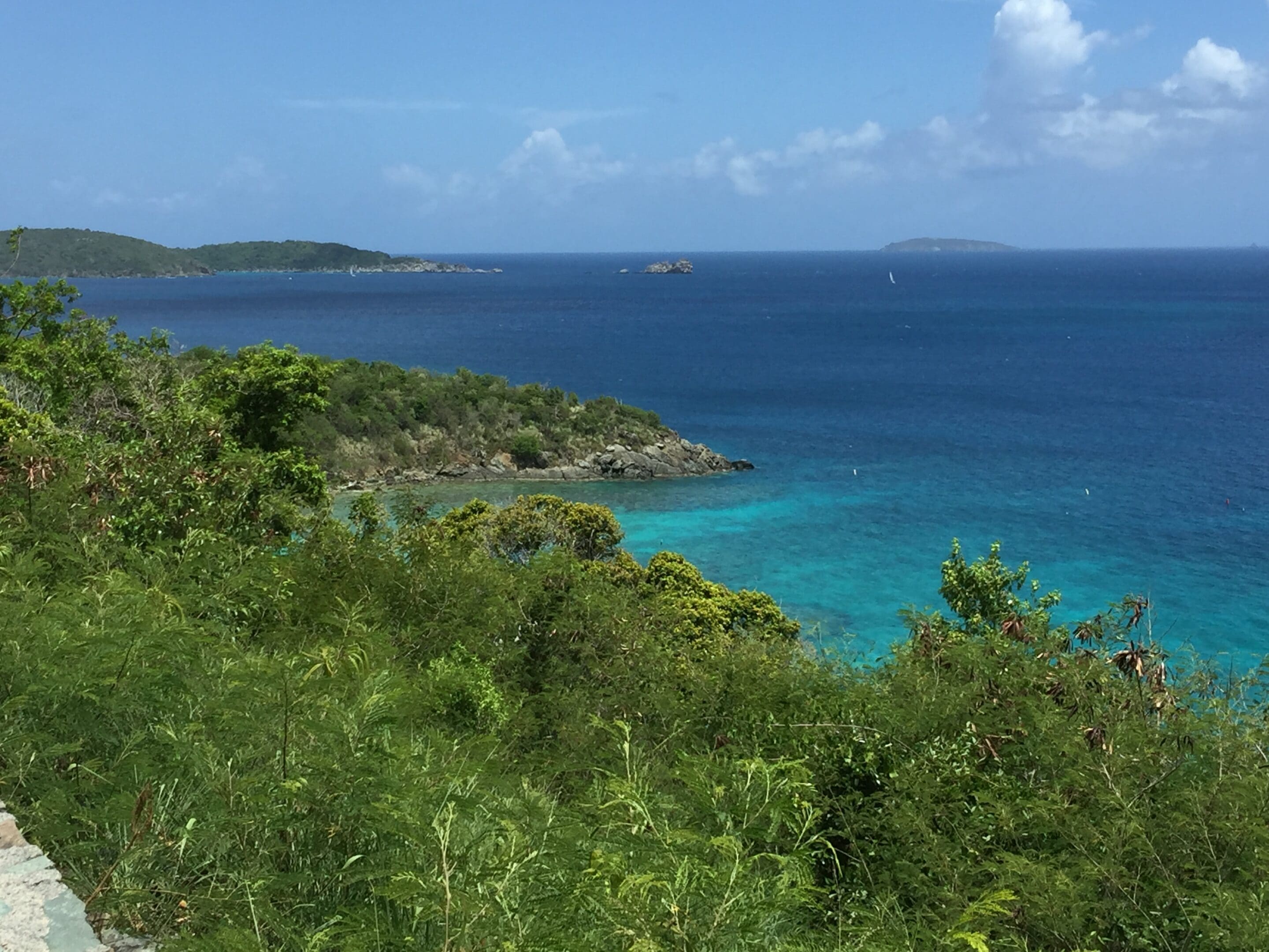 Lush green hillside overlooking a vibrant blue ocean under a partly cloudy sky.
