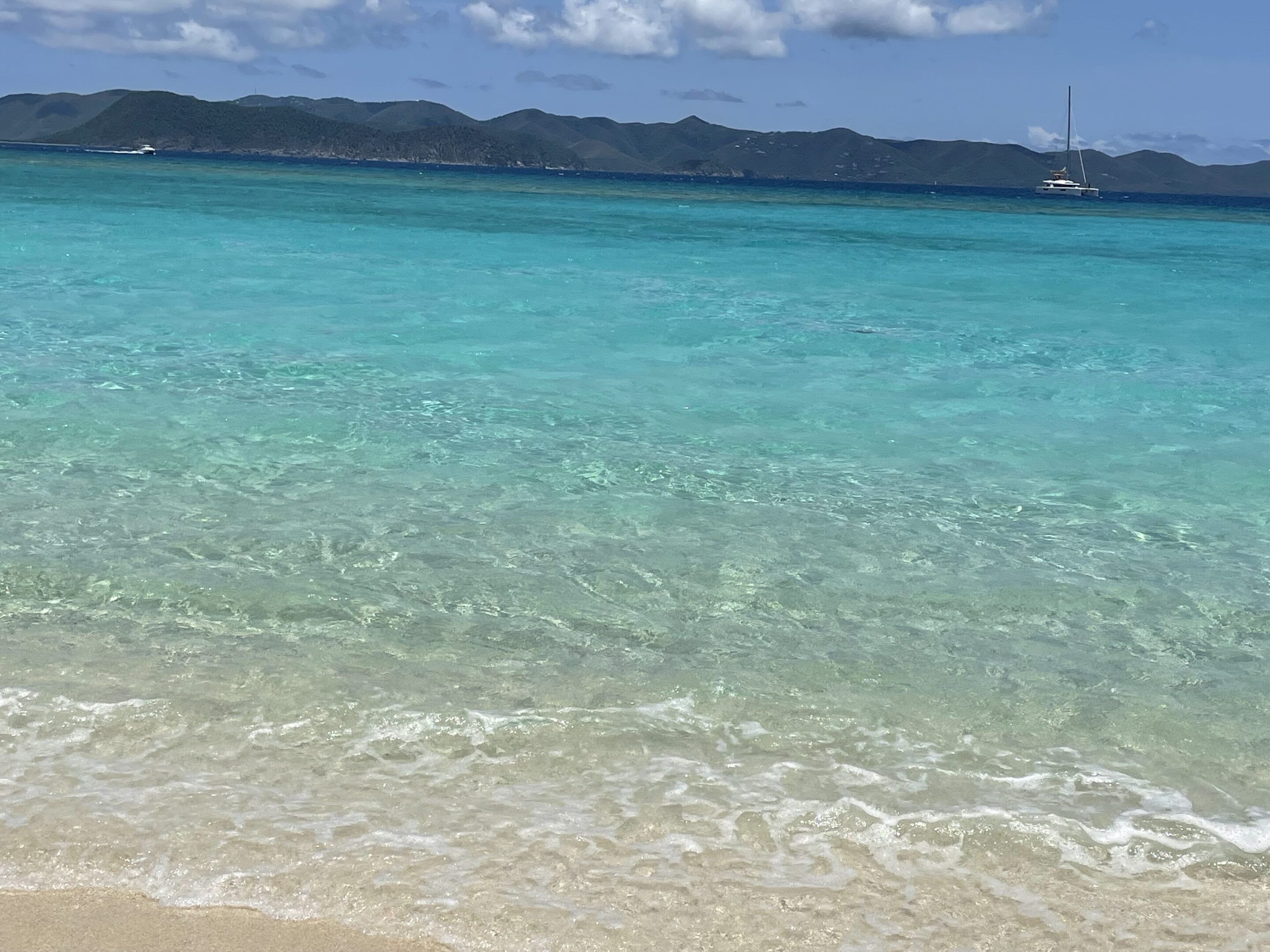 Clear turquoise water gently laps a sandy beach under a blue sky.
