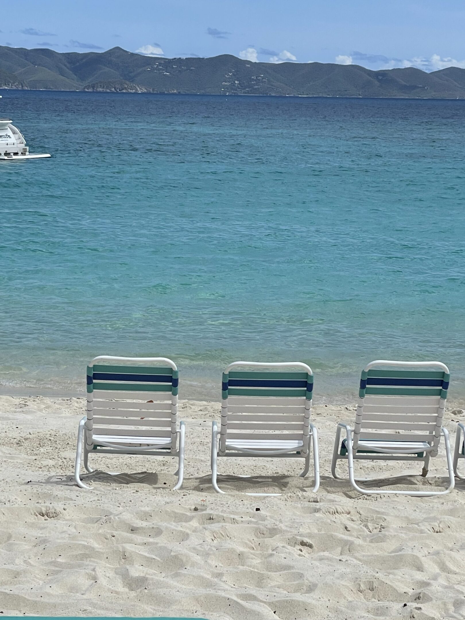 Three empty lounge chairs facing the calm blue sea on a sandy beach.