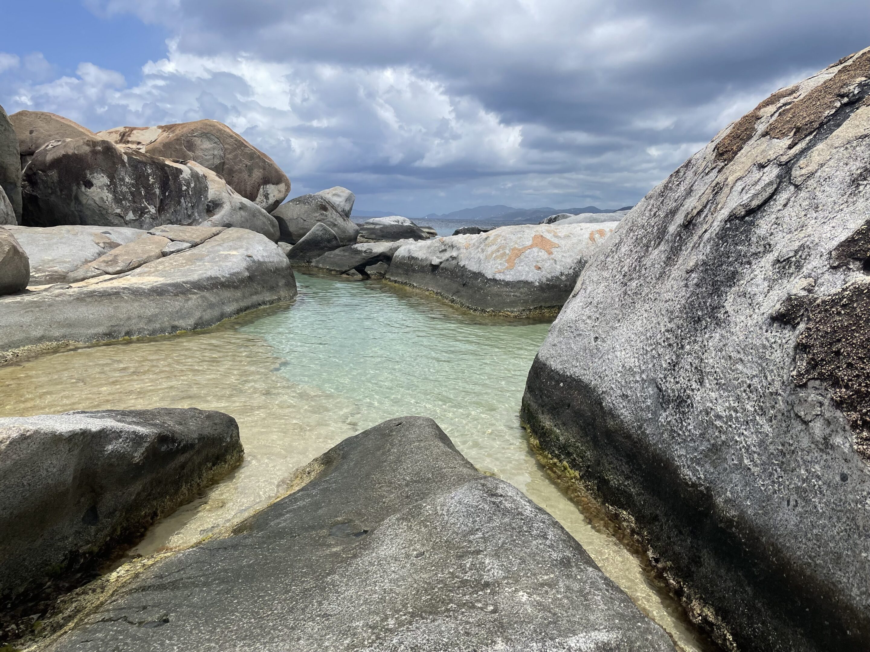 A serene rocky pool with clear water under a cloudy sky.