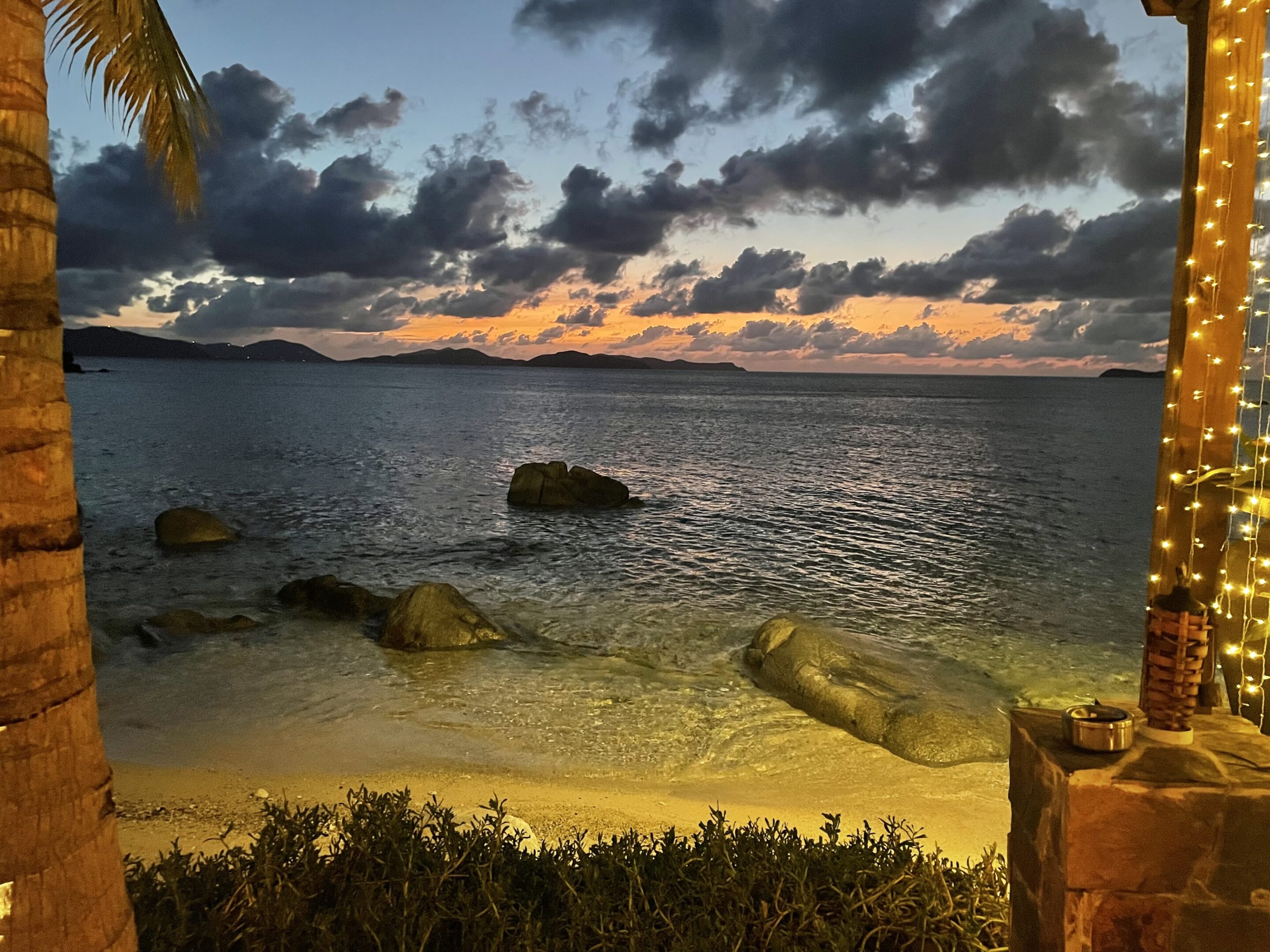 Sunset over a calm beach with scattered clouds.