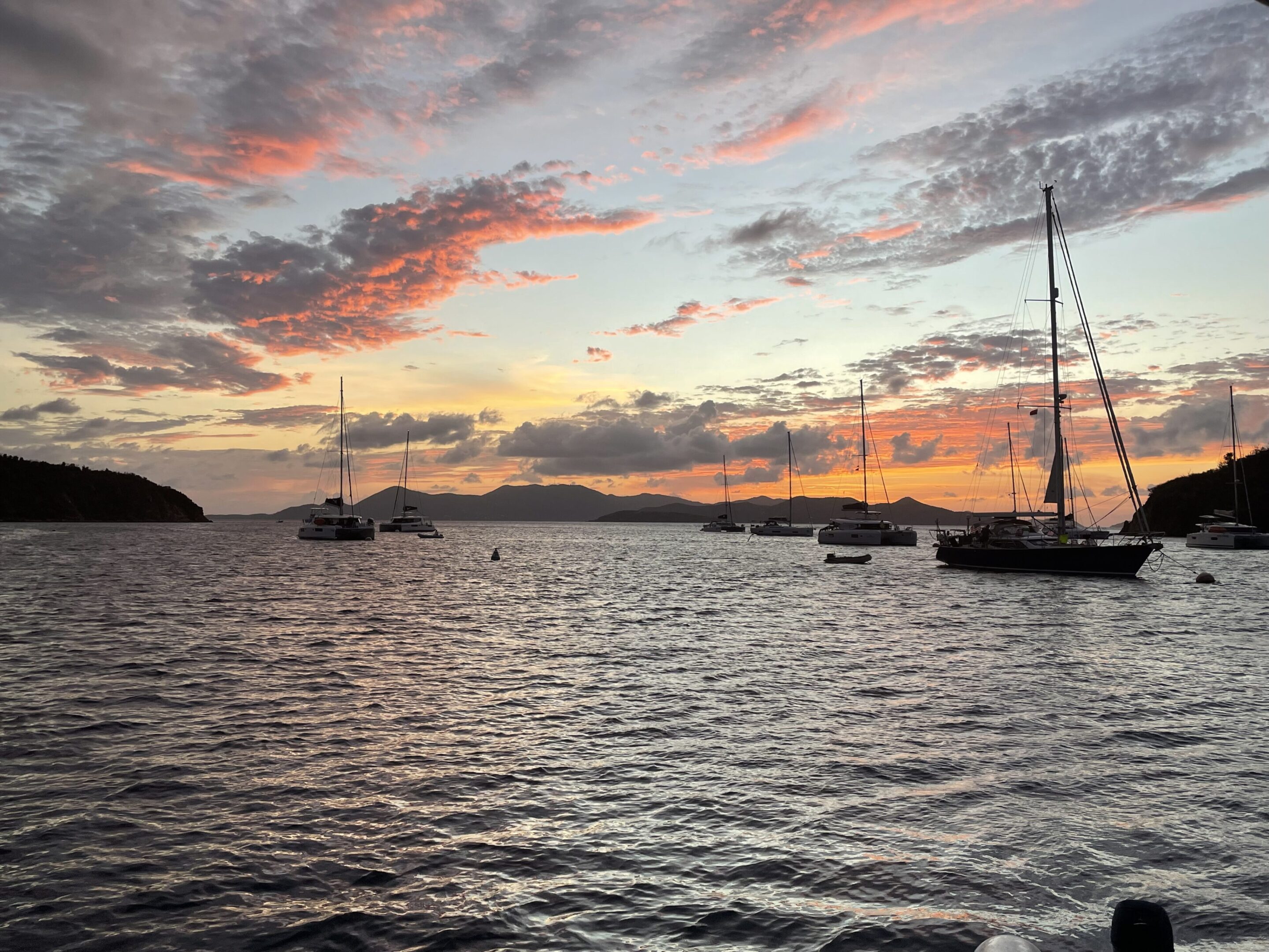 Sailboats anchored on calm water during a colorful sunset.