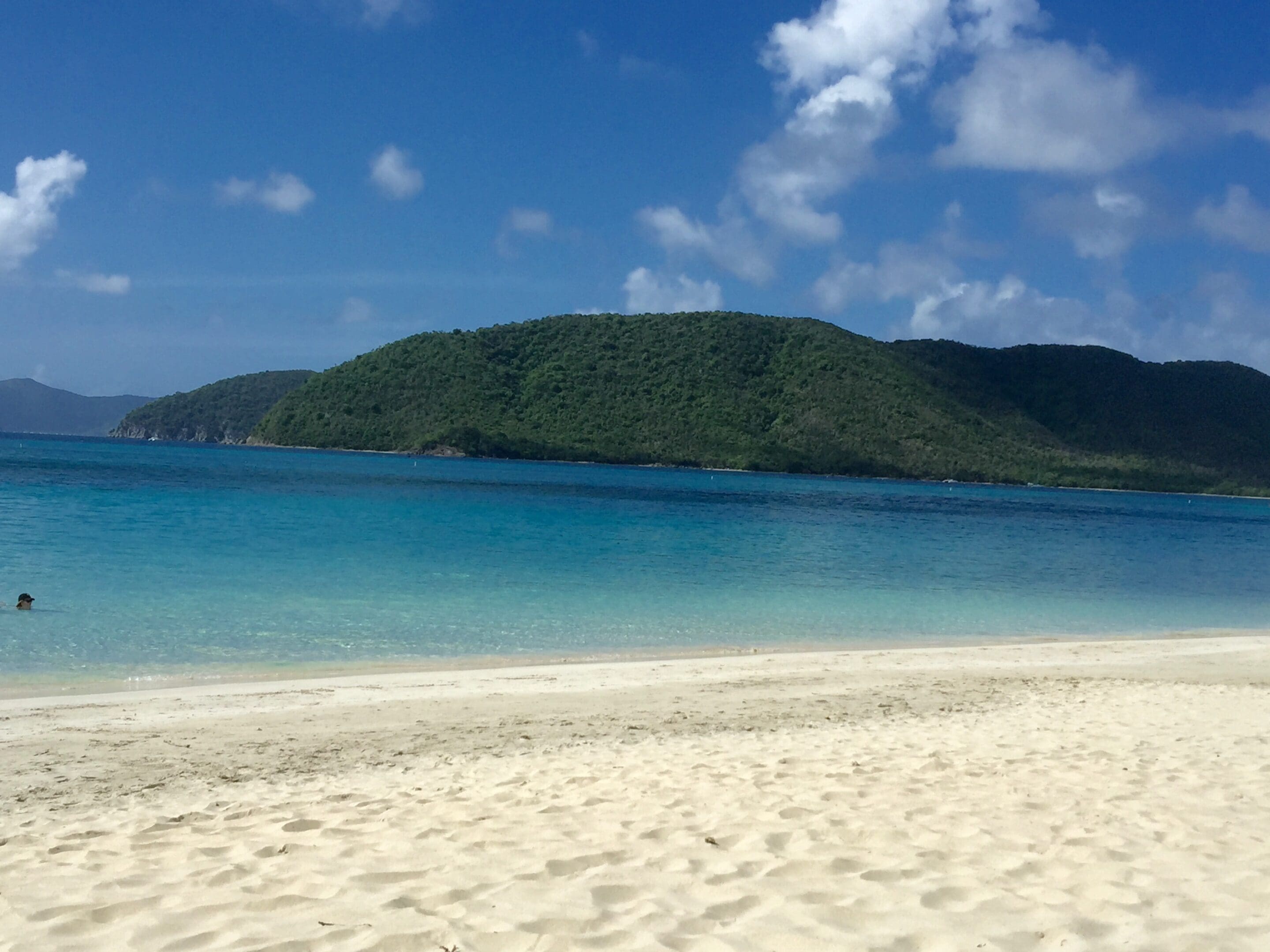 Pristine sandy beach with turquoise water and green hills under a blue sky.