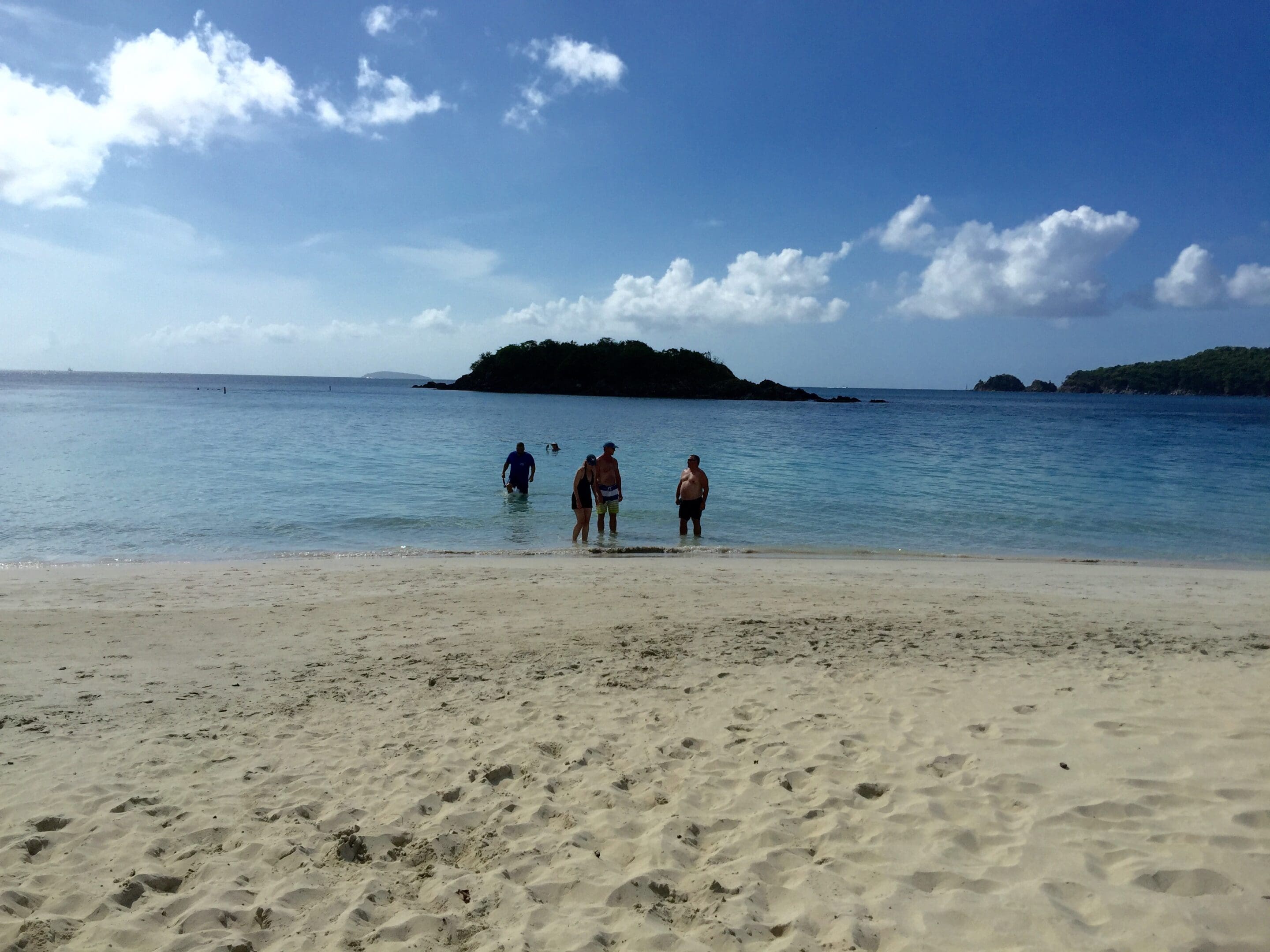 People enjoying a sunny day at a sandy beach with a small island in the distance.